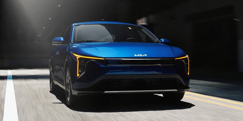 Front view of a blue Kia SUV driving on a road.