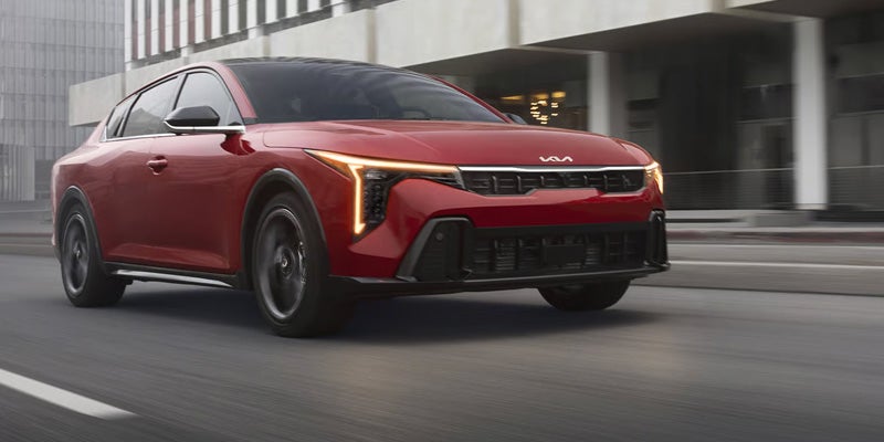 Front view of a red 2026 Kia K4 sedan driving on a city street.