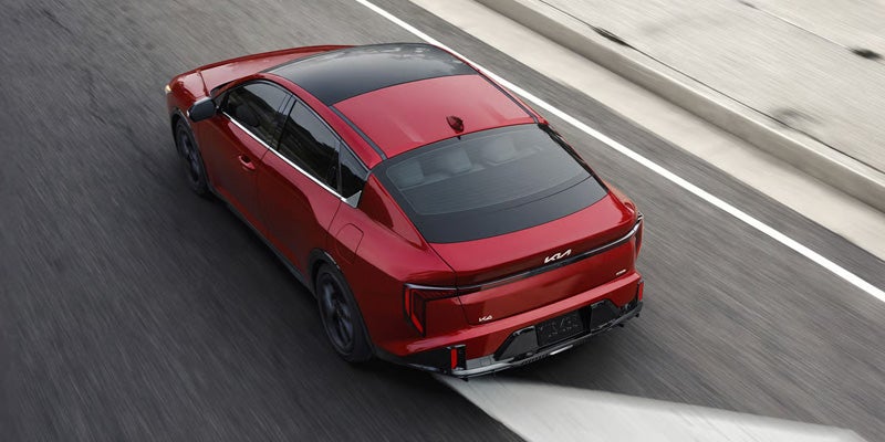 Rear view of a red 2026 Kia K4 sedan driving on a road.